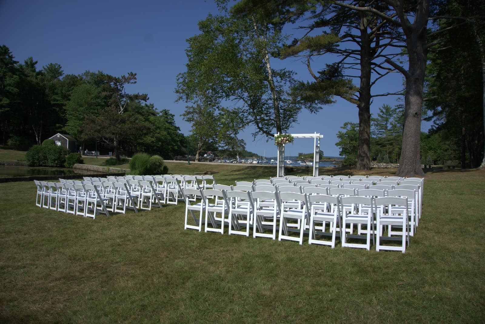 Rows of white chairs set for an outdoor wedding ceremony beside a New England harbor
