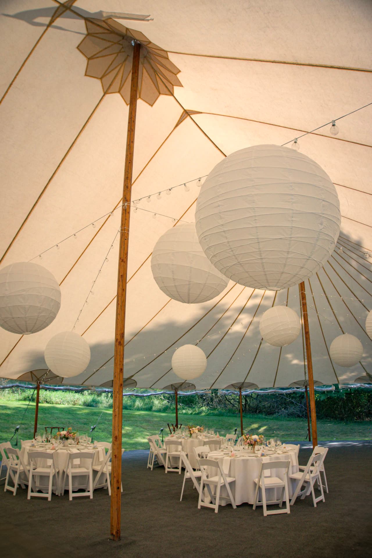 Paper lanterns hung inside a sailcloth tent, tables set for a reception below